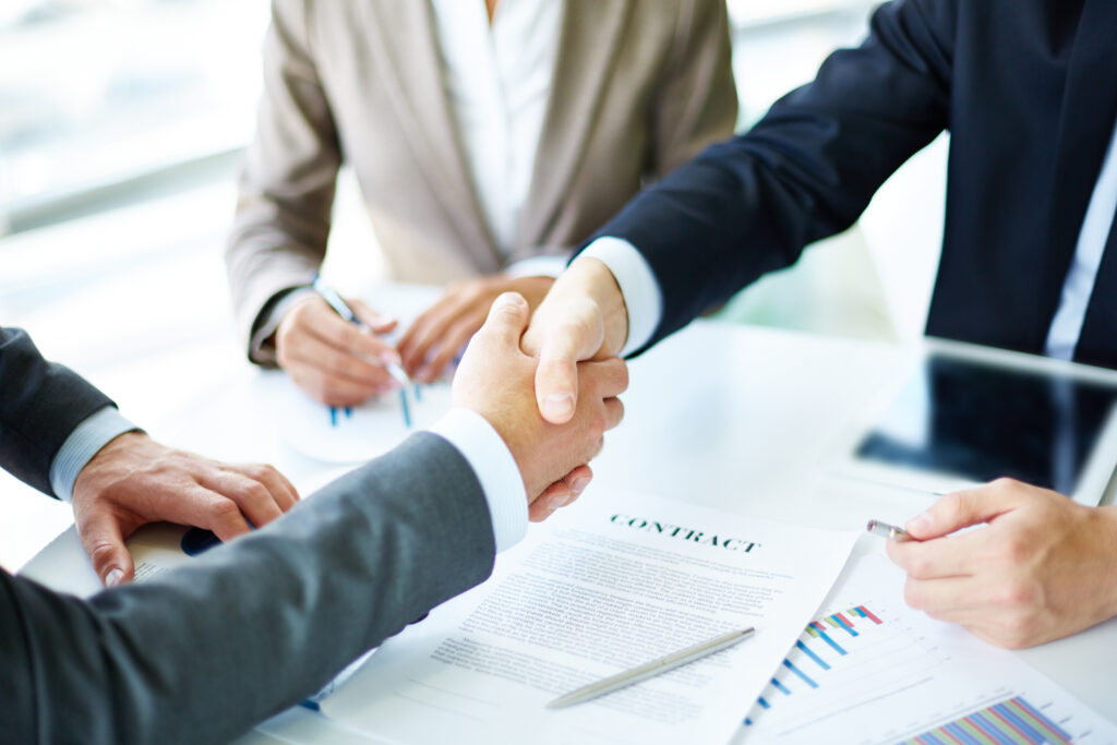 Image of business partners handshaking over a stack of papers with CONTRACT written on the top page