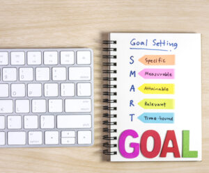 smart goals setting written on the notebook and keyboard over wooden table