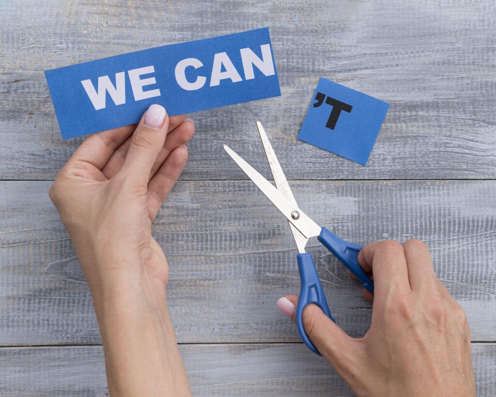 A set of human hands holding a pair of scissors in the right hand and the words "we can" in the left hand. It appears that the 't has been cut off of the phrase "we can't"