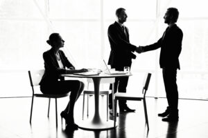 Businesswoman seated at round table watching two men shake hands