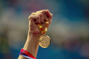 hand of a woman raising an Olympic gold medal in victory